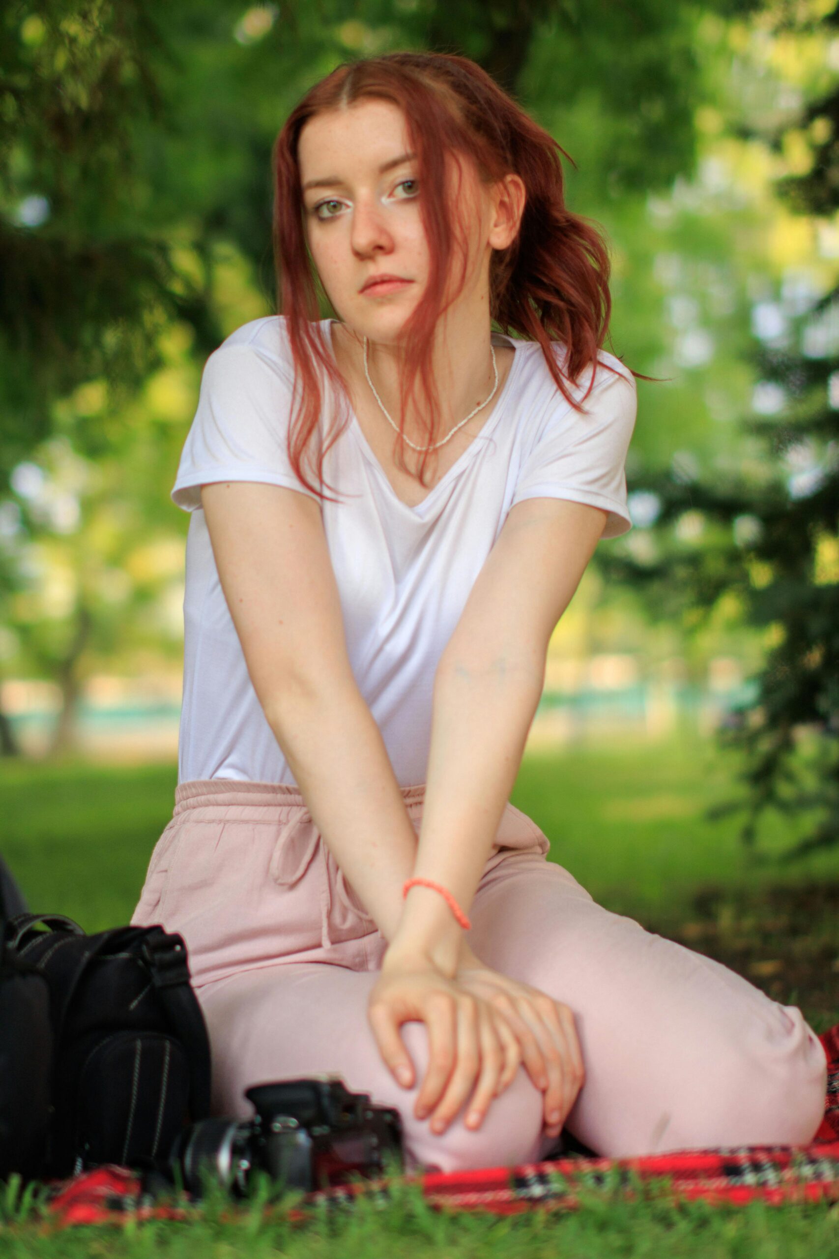 Young redhead woman in casual attire sitting in park. Relaxed outdoor lifestyle setting.