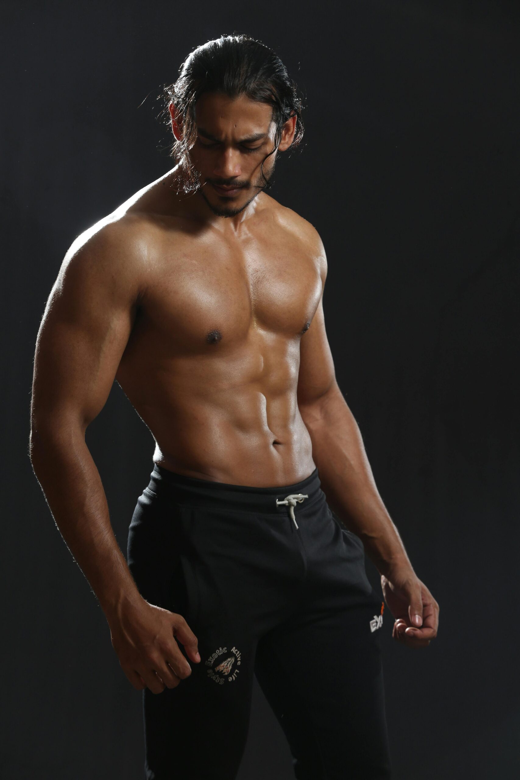 A muscular man posing shirtless in a studio shoot, showcasing fitness and strength.