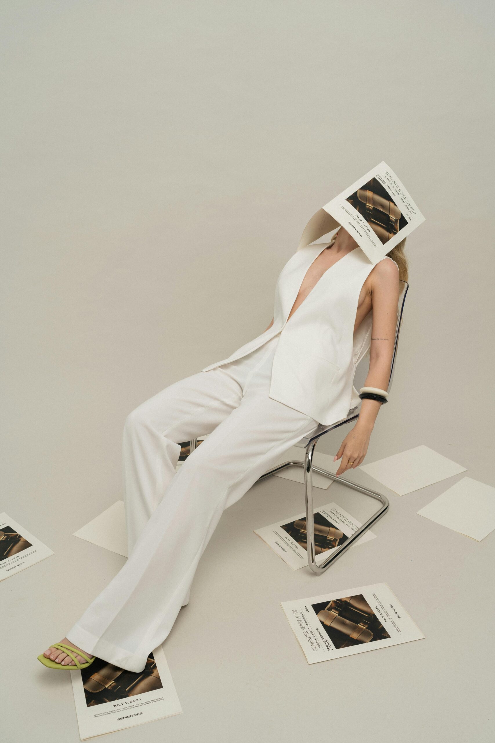 Fashionable woman in white attire poses in a studio with scattered papers.
