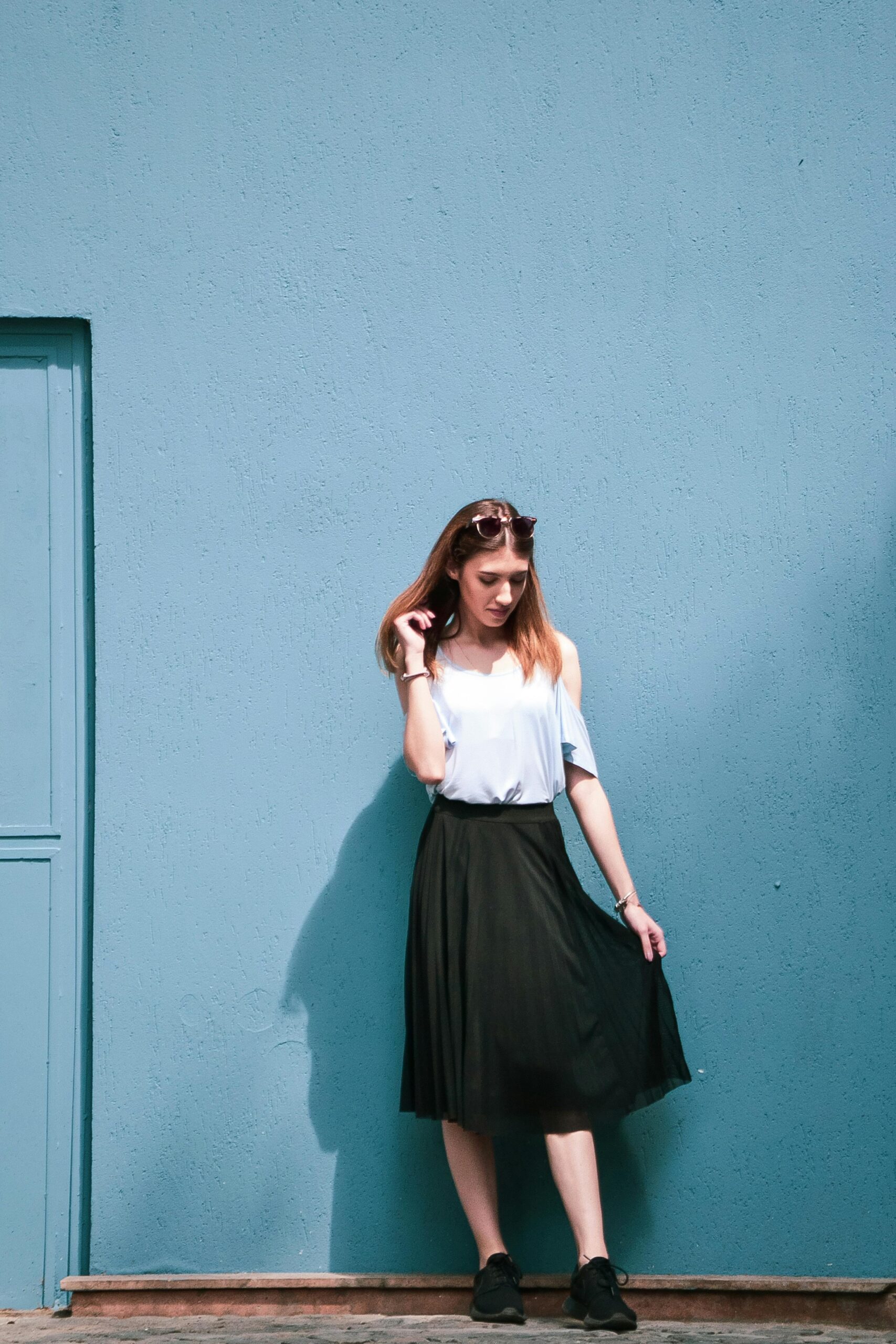 Fashionable woman in summer outfit posing against a textured blue wall outdoors.